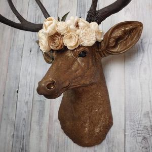 Faux taxidermy deer head that's been painted antique gold with chestnut brown accenting. The antlers are chestnut brown and atop the deers head is a cream floral crown made out of wooden sola flowers