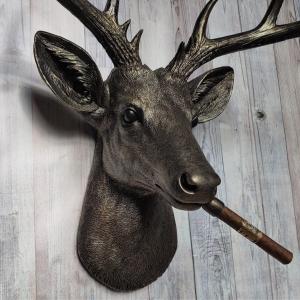 Faux taxidermy deer head painted rubbed bronze with rubbed bronze antlers and gold accents. A cigar is in the deers mouth.