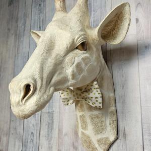 faux taxidermy giraffe head wall mount with a bow tie around it's neck.