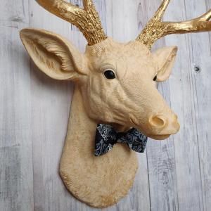 Faux taxidermy deer head painted cream with gold accenting and gold antlers. A fabric bow tie accents the neck, fabric color is dark blue multi with lighter blue and white