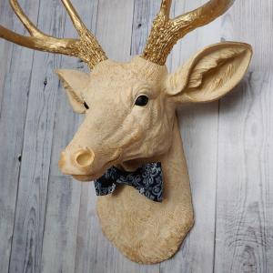 Faux taxidermy deer head painted cream with gold accenting and gold antlers. A fabric bow tie accents the neck, fabric color is dark blue multi with lighter blue and white