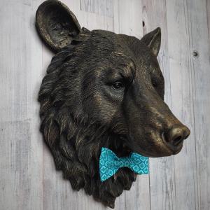 Faux taxidermy bear head wall mount, painted black with gold accenting. A turquoise and blue fabric bow tie accents the bears neck.