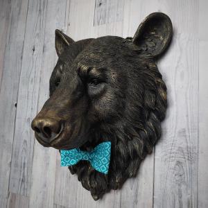 Faux taxidermy bear head wall mount, painted black with gold accenting. A turquoise and blue fabric bow tie accents the bears neck.