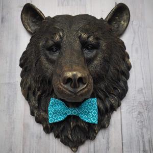 Faux taxidermy bear head wall mount, painted black with gold accenting. A turquoise and blue fabric bow tie accents the bears neck.