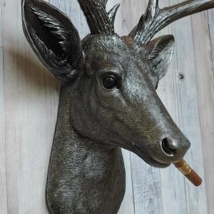 Faux taxidermy deer head painted rubbed bronze with rubbed bronze antlers and silver accents. A cigar is in the deers mouth.