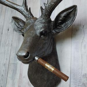 Faux taxidermy deer head painted rubbed bronze with rubbed bronze antlers and silver accents. A cigar is in the deers mouth.