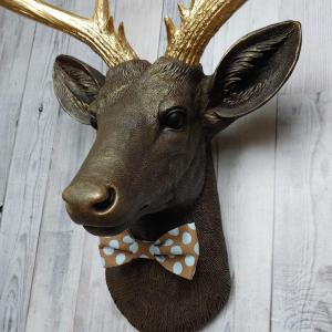 Faux taxidermy deer head. Painted chestnut brown with gold accents and gold antlers. There is a blue and brown polka dot bow tie on the deers neck.