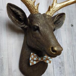 Faux taxidermy deer head. Painted chestnut brown with gold accents and gold antlers. There is a blue and brown polka dot bow tie on the deers neck.