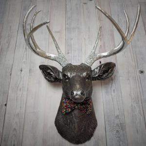 Faux taxidermy deer head painted rubbed bronze with silver accents and silver antlers. The deer has a bow tie on it's neck in black with colorful sprinkles.