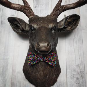 Faux taxidermy deer head, painted rubbed bronze with dark copper accenting on the head, antlers are dark copper. Removable bow tie, fabric is black with multi colored sprinkles.
