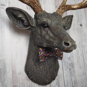 Faux taxidermy dee head painted chestnut brown and accented with antique white and antique gold. The antlers have been painted antique gold and the eyes have been painted black. A fabric bow tie that has a black background with multi colored sprinkles accents the deers neck.