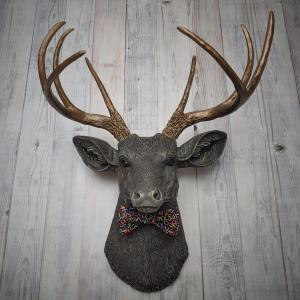 Faux taxidermy dee head painted chestnut brown and accented with antique white and antique gold. The antlers have been painted antique gold and the eyes have been painted black. A fabric bow tie that has a black background with multi colored sprinkles accents the deers neck.