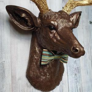 Faux taxidermy deer head painted dark copper with gold accents and gold antlers. A striped bow tie is at the neck.