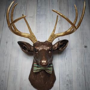 Faux taxidermy deer head painted dark copper with gold accents and gold antlers. A striped bow tie is at the neck.