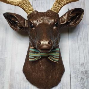 Faux taxidermy deer head painted dark copper with gold accents and gold antlers. A striped bow tie is at the neck.