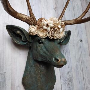 Faux taxidermy deer head painted verdigris with antique gold antlers. A floral crown made of cream sola flowers rests atop the deers head