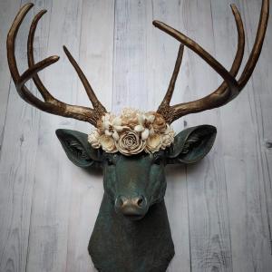 Faux taxidermy deer head painted verdigris with antique gold antlers. A floral crown made of cream sola flowers rests atop the deers head