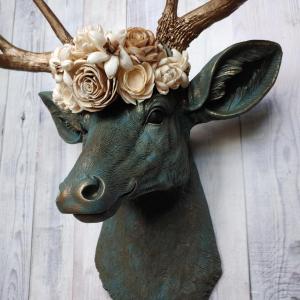 Faux taxidermy deer head painted verdigris with antique gold antlers. A floral crown made of cream sola flowers rests atop the deers head