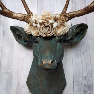 Faux taxidermy deer head painted verdigris with antique gold antlers. A floral crown made of cream sola flowers rests atop the deers head