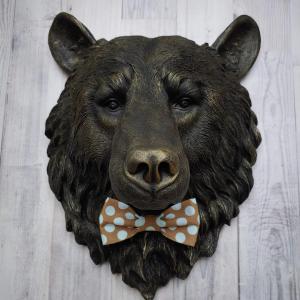 Faux taxidermy bear head wall mount, painted black with gold accenting. A brown and blue polka dot fabric bow tie accents the bears neck
