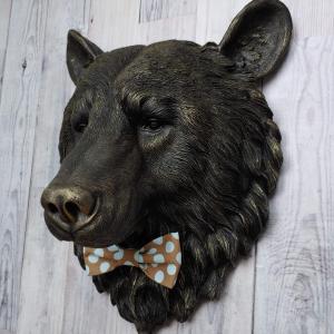 Faux taxidermy bear head wall mount, painted black with gold accenting. A brown and blue polka dot fabric bow tie accents the bears neck