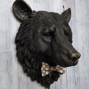 Faux taxidermy bear head wall mount, painted black with gold accenting. A brown and blue polka dot fabric bow tie accents the bears neck
