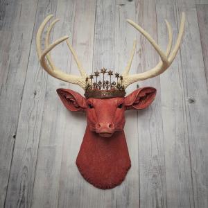 Faux taxidermy deer head, painted red with antique white antlers with a bronze Santos crown atop its head.