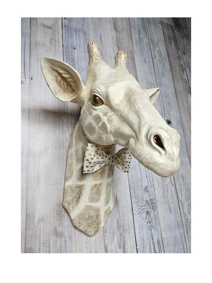 faux taxidermy giraffe head , painted antique white and gold with bronze accents. a white and gold polka dot bow tie accents the giraffes neck.
