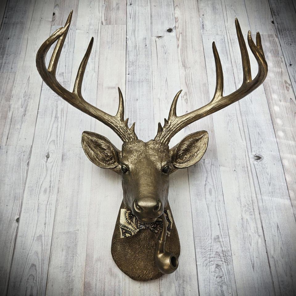 Faux taxidermy deer head with smoking pipe and bow tie, painted antique gold with dark bronze accents.