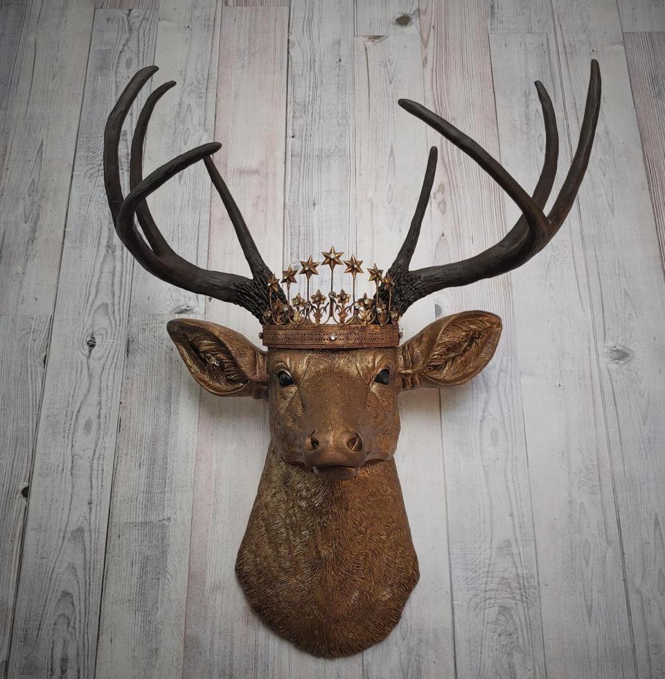 Faux taxidermy deer head that's been painted antique gold with chestnut brown accenting. The antlers are chestnut brown and a vintage inspired Santos star crown/tiara sits arop the deers head.