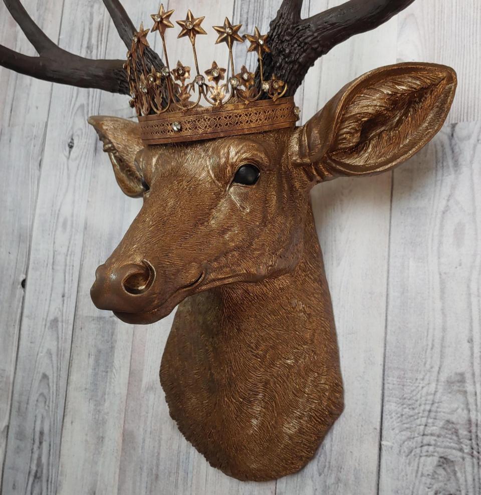 Faux taxidermy deer head that's been painted antique gold with chestnut brown accenting. The antlers are chestnut brown and a vintage inspired Santos star crown/tiara sits arop the deers head.