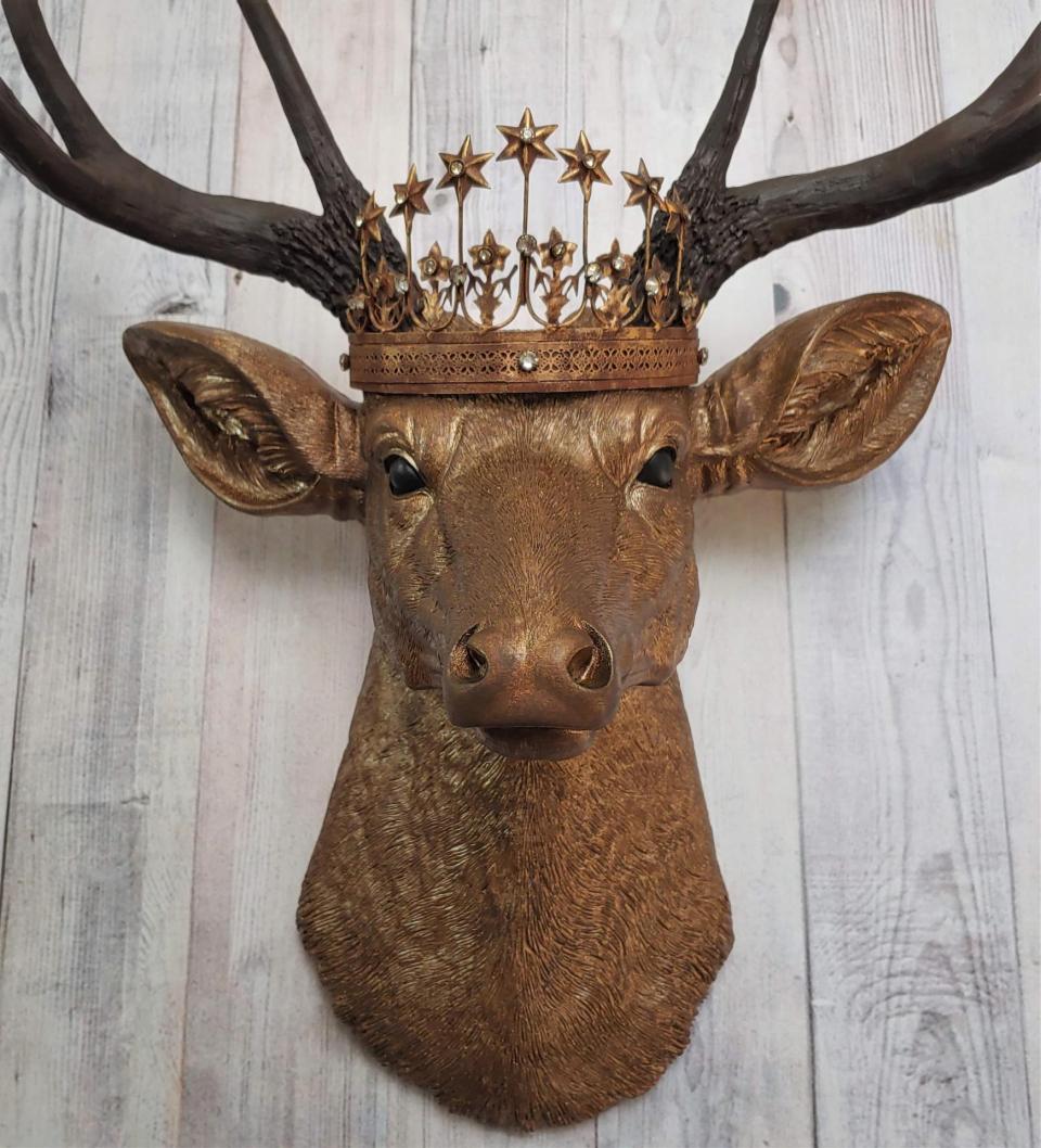 Faux taxidermy deer head that's been painted antique gold with chestnut brown accenting. The antlers are chestnut brown and a vintage inspired Santos star crown/tiara sits arop the deers head.