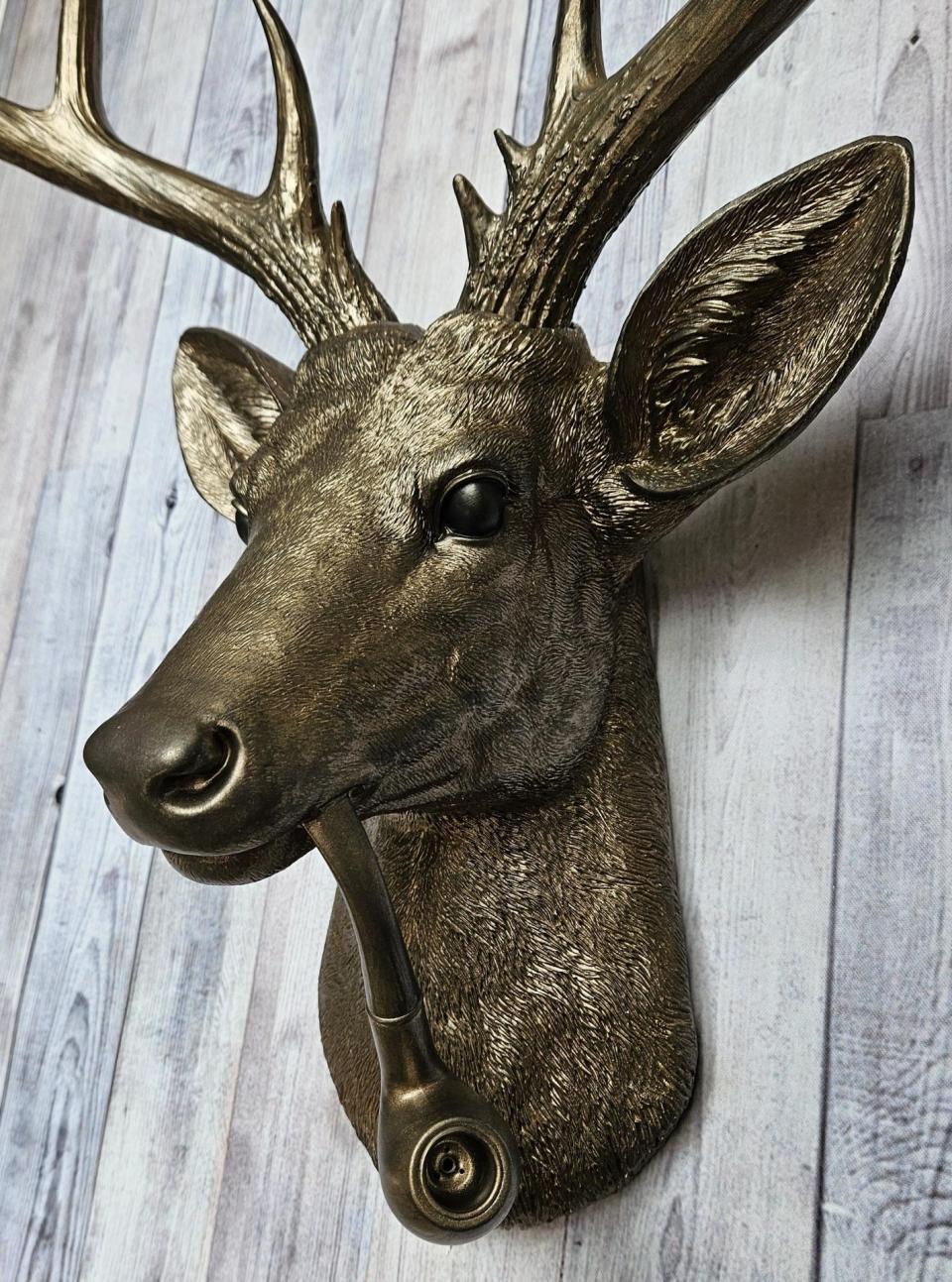 Faux taxidermy deer head wall mount with smoking pipe, painted antique gold with dark bronze accenting.