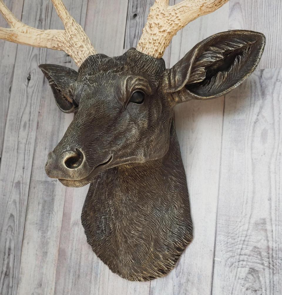 Faux taxidermy deer head painted chestnut brown with cream and gold accenting. Cream antlers with gold antlers, a brass bird rests atop one of the antlers.