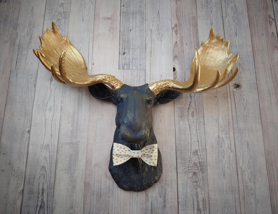 Faux taxidermy moose head painted midnight blue with metallic gold antlers. A white and gold polka dot bow tie accents the neck of the moose.