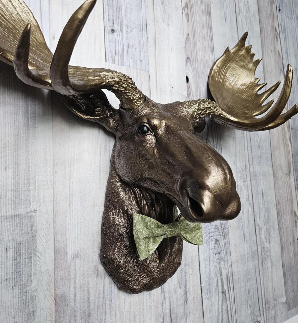 faux taxidermy moose head wall mount, painted dark copper with antique gold accents and antique gold antlers. A green bow tie accents the neck.
