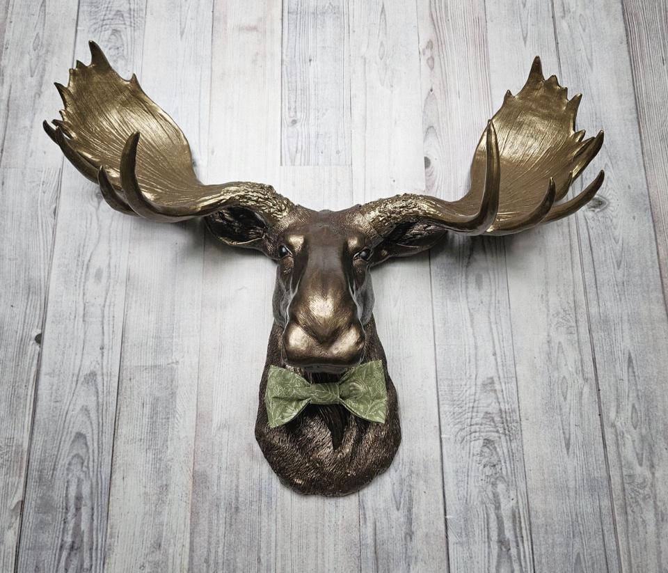 faux taxidermy moose head wall mount, painted dark copper with antique gold accents and antique gold antlers. A green bow tie accents the neck.