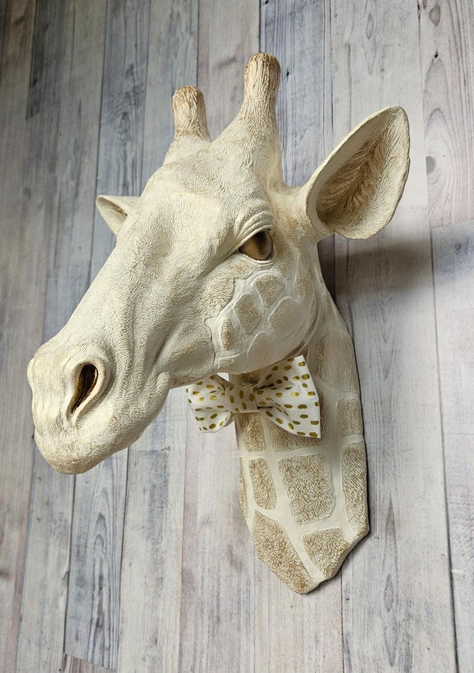 faux taxidermy giraffe head wall mount with a bow tie around it's neck.