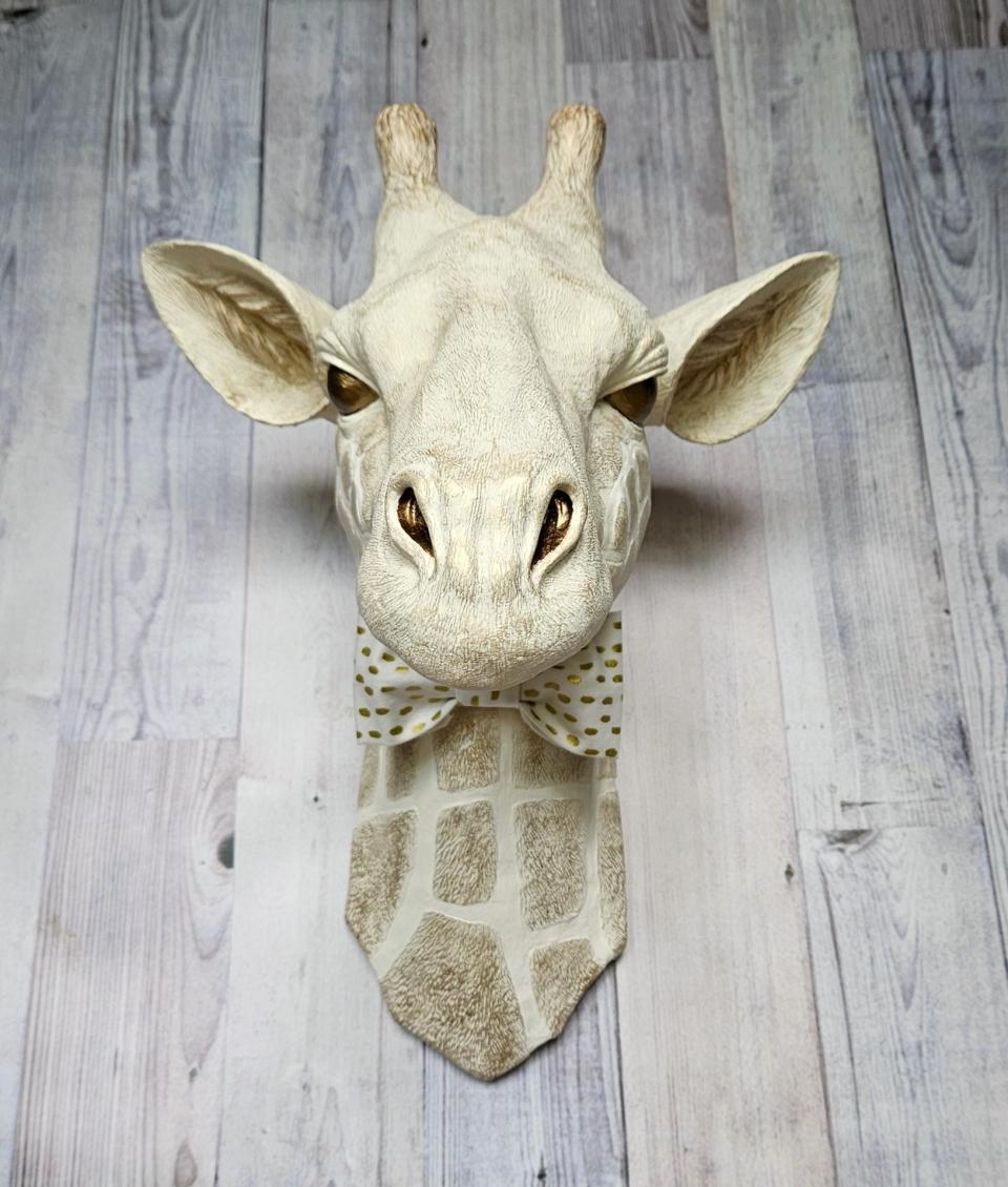 faux taxidermy giraffe head wall mount with a bow tie around it's neck.
