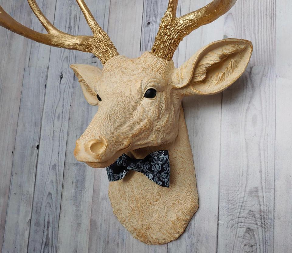 Faux taxidermy deer head painted cream with gold accenting and gold antlers. A fabric bow tie accents the neck, fabric color is dark blue multi with lighter blue and white