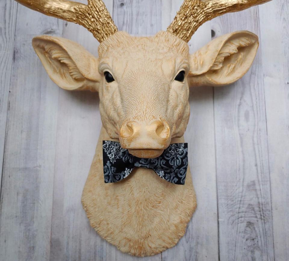 Faux taxidermy deer head painted cream with gold accenting and gold antlers. A fabric bow tie accents the neck, fabric color is dark blue multi with lighter blue and white