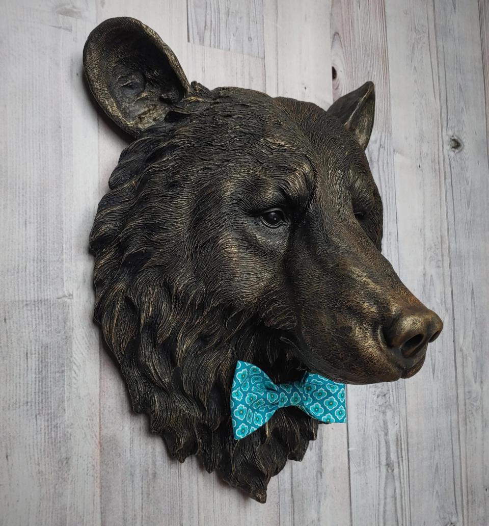 Faux taxidermy bear head wall mount, painted black with gold accenting. A turquoise and blue fabric bow tie accents the bears neck.