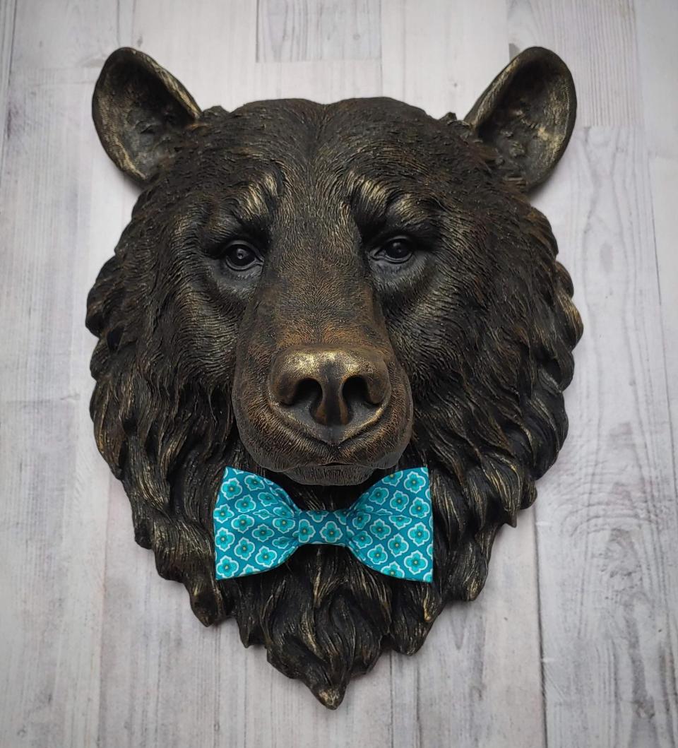 Faux taxidermy bear head wall mount, painted black with gold accenting. A turquoise and blue fabric bow tie accents the bears neck.