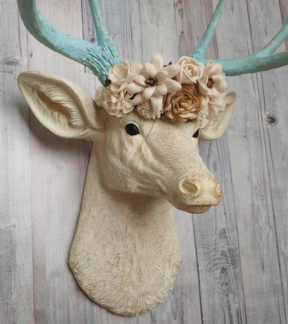 Faux taxidermy deer head, painted antique white with spa blue and gold accents. Antlers are spa blue with gold accents. A removable floral crown made out of cream sola flowers rests atop the deer head