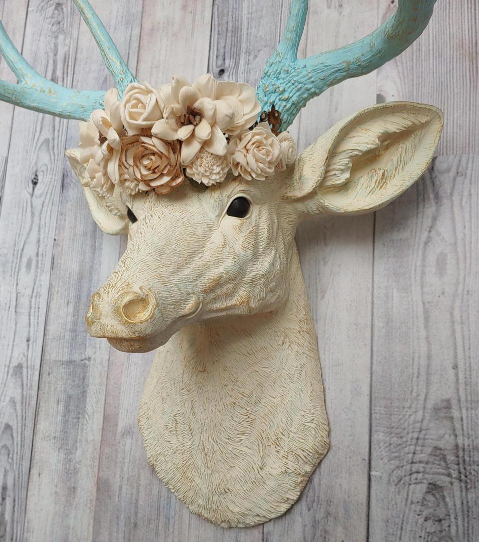 Faux taxidermy deer head, painted antique white with spa blue and gold accents. Antlers are spa blue with gold accents. A removable floral crown made out of cream sola flowers rests atop the deer head