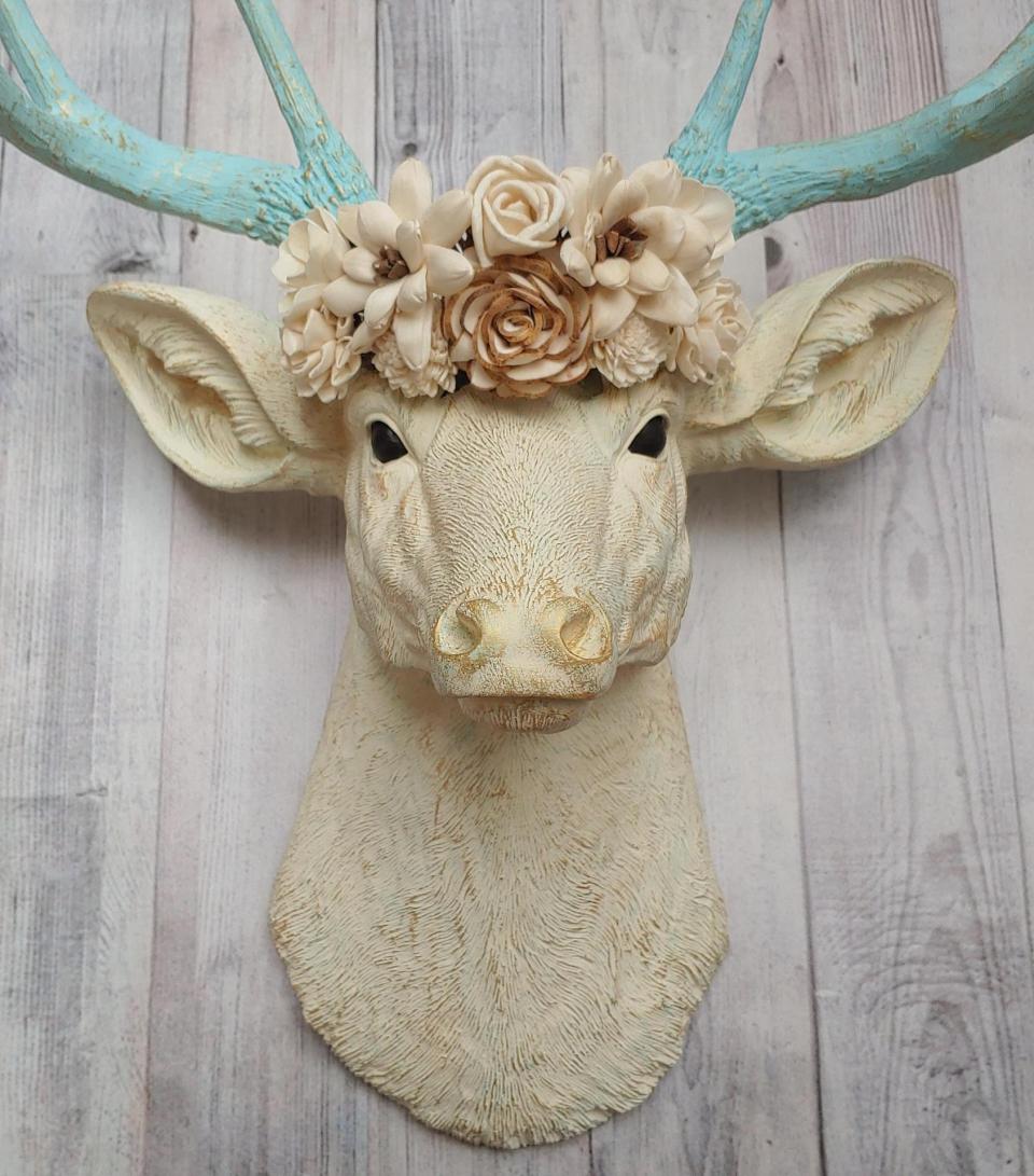 Faux taxidermy deer head, painted antique white with spa blue and gold accents. Antlers are spa blue with gold accents. A removable floral crown made out of cream sola flowers rests atop the deer head