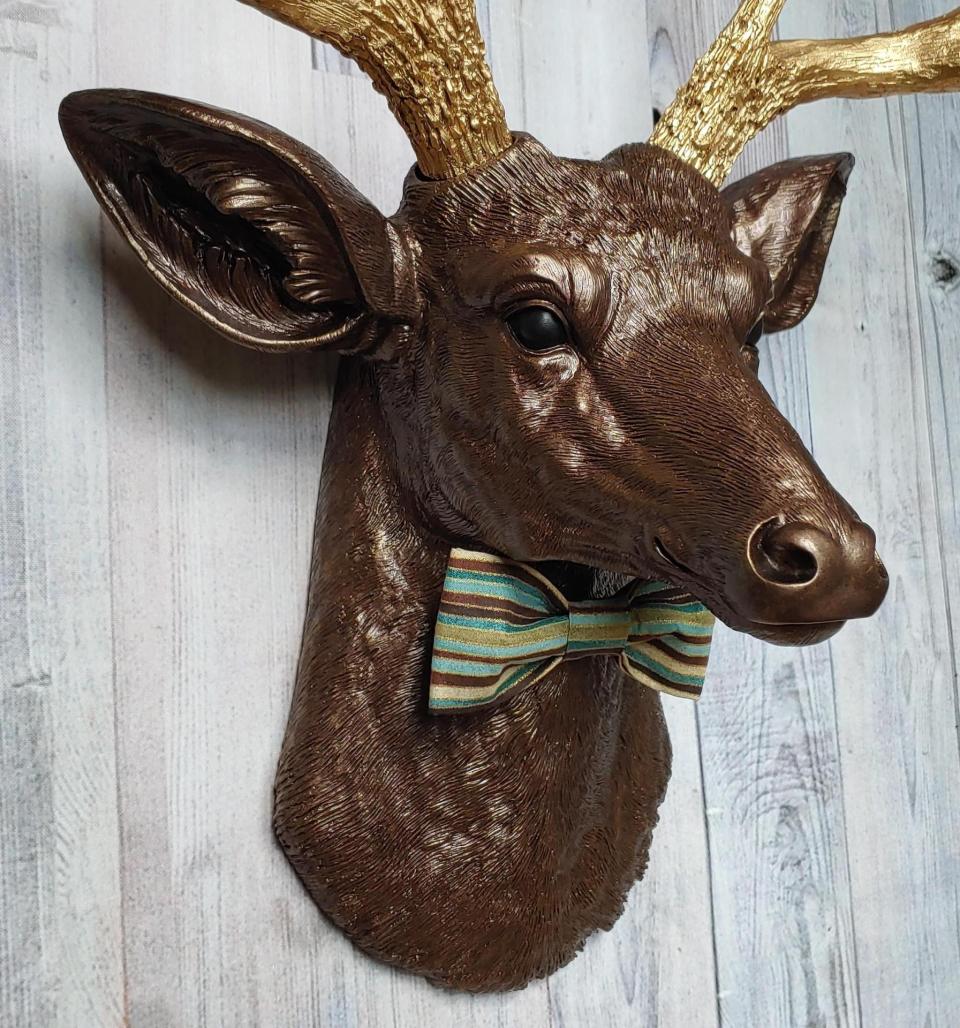 Faux taxidermy deer head painted dark copper with gold accents and gold antlers. A striped bow tie is at the neck.