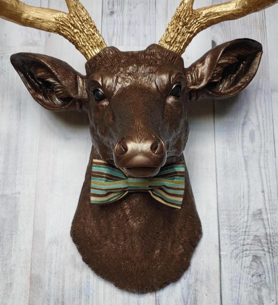 Faux taxidermy deer head painted dark copper with gold accents and gold antlers. A striped bow tie is at the neck.