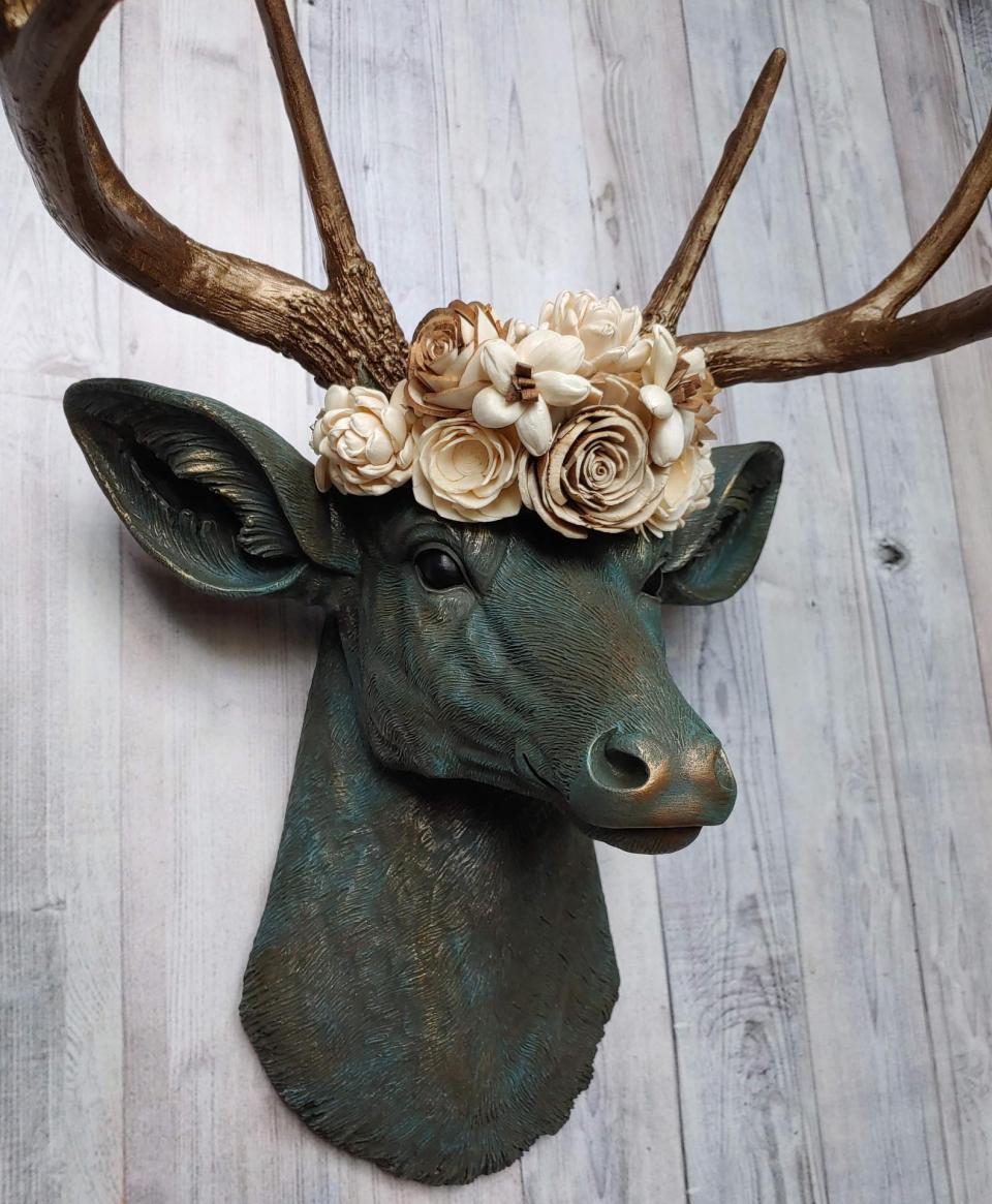Faux taxidermy deer head painted verdigris with antique gold antlers. A floral crown made of cream sola flowers rests atop the deers head