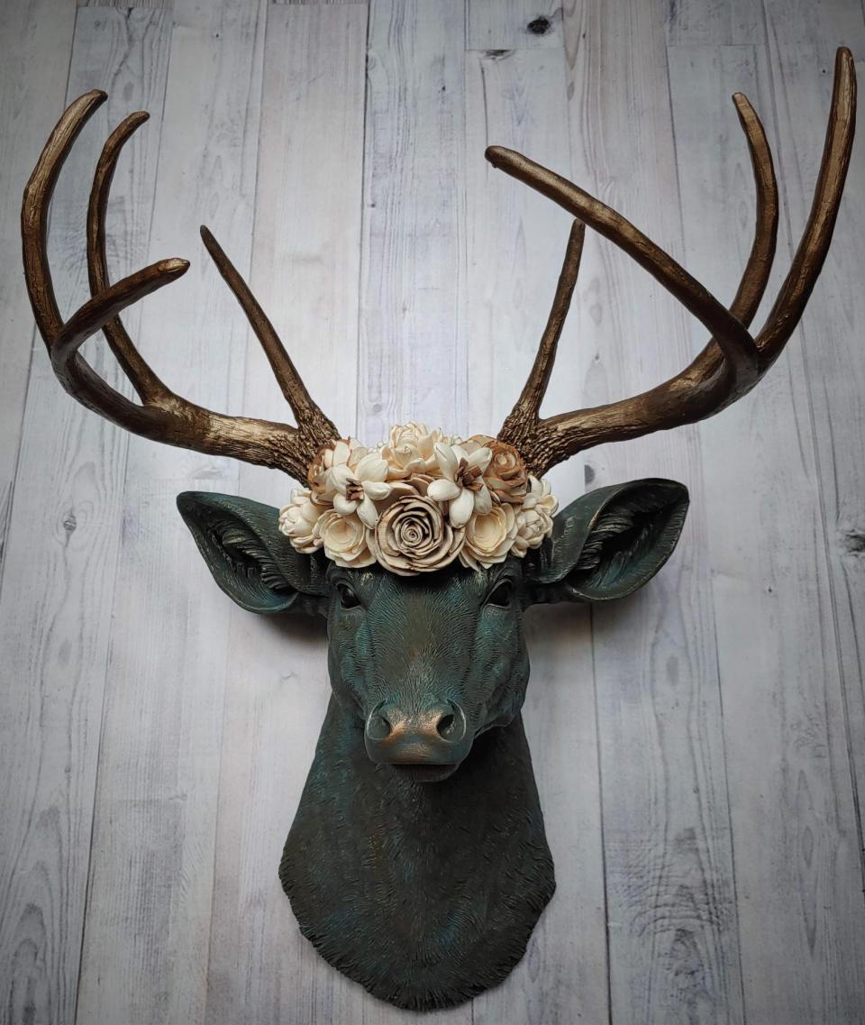 Faux taxidermy deer head painted verdigris with antique gold antlers. A floral crown made of cream sola flowers rests atop the deers head